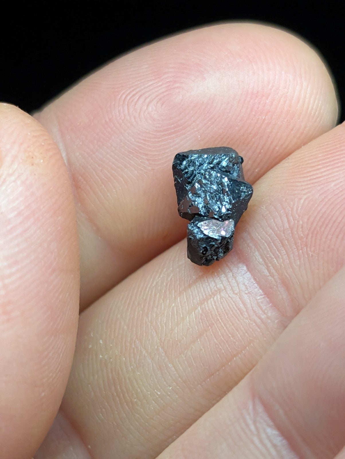 A small, dark metallic mineral specimen with a rough, jagged surface and subtle iridescent highlights.