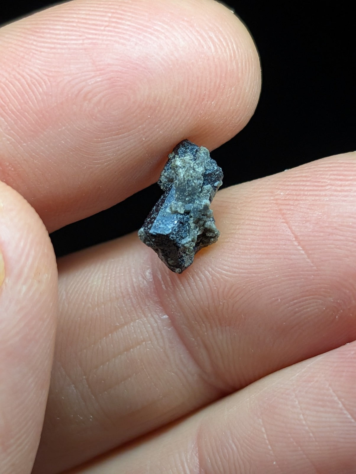 A small, irregularly shaped mineral specimen with a dark blue to black surface and subtle greenish veining.