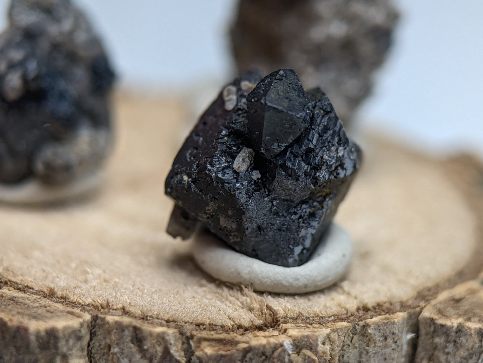 Set of 3 brookite and smoky quartz minerals from magnet cove arkansas with dark faceted crystals and metallic sheen on wood stand