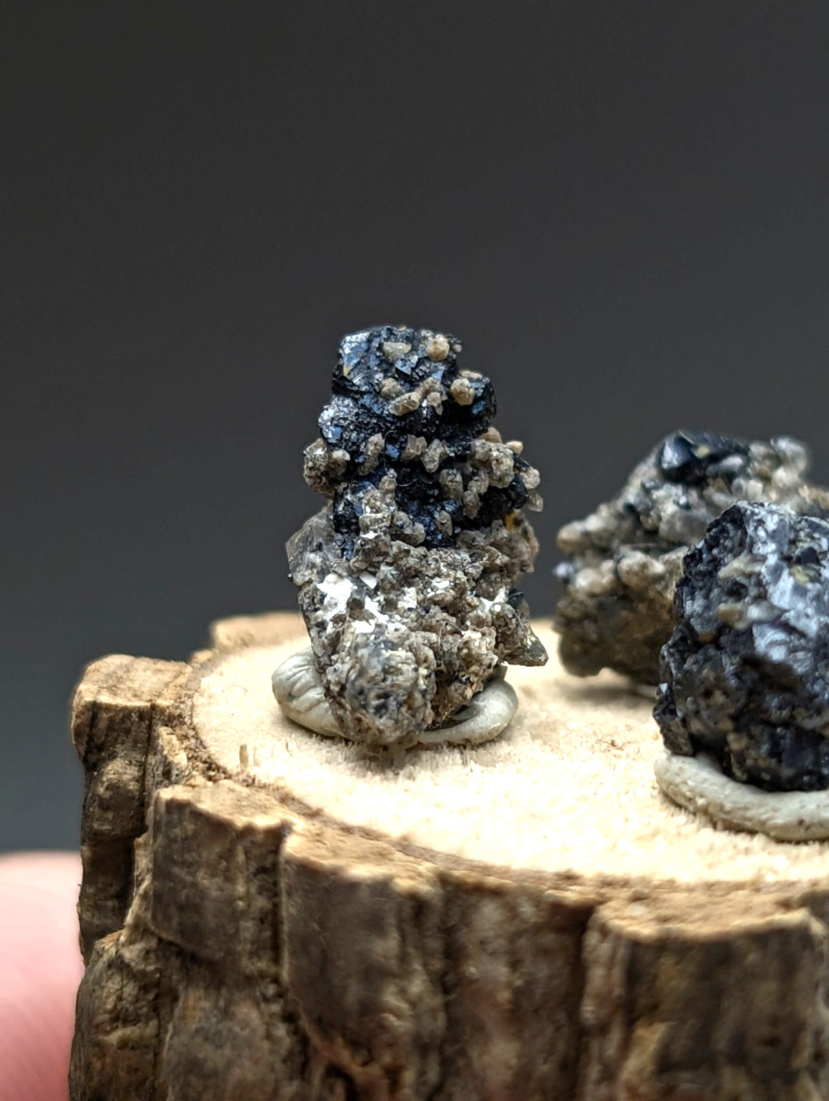 A dark textured brookite and smoky quartz mineral specimen with rough clustered surface on a rustic wood stand