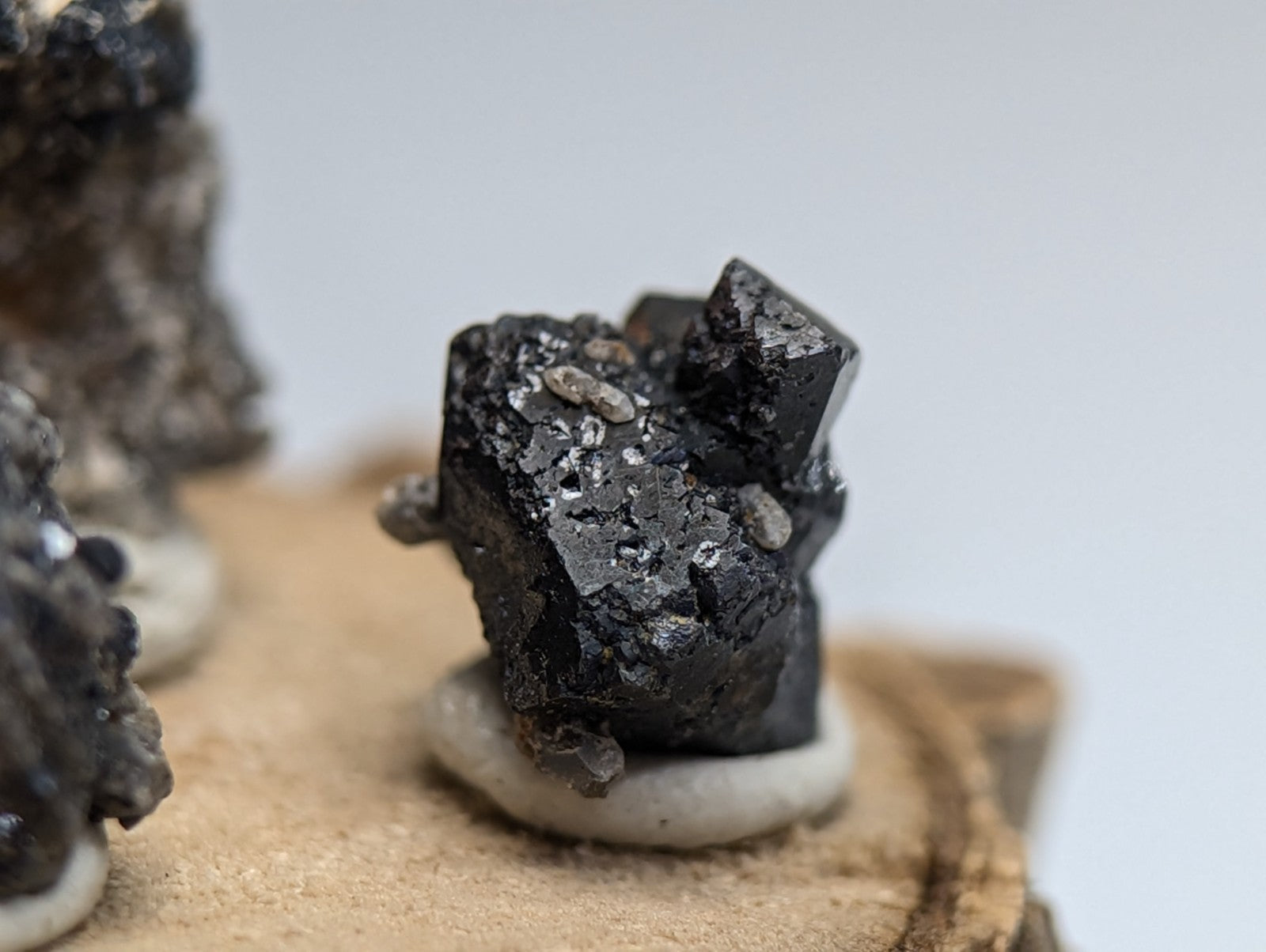 Set of 3 brookite and smoky quartz mineral specimens with dark rough texture and lighter inclusions on wood stand