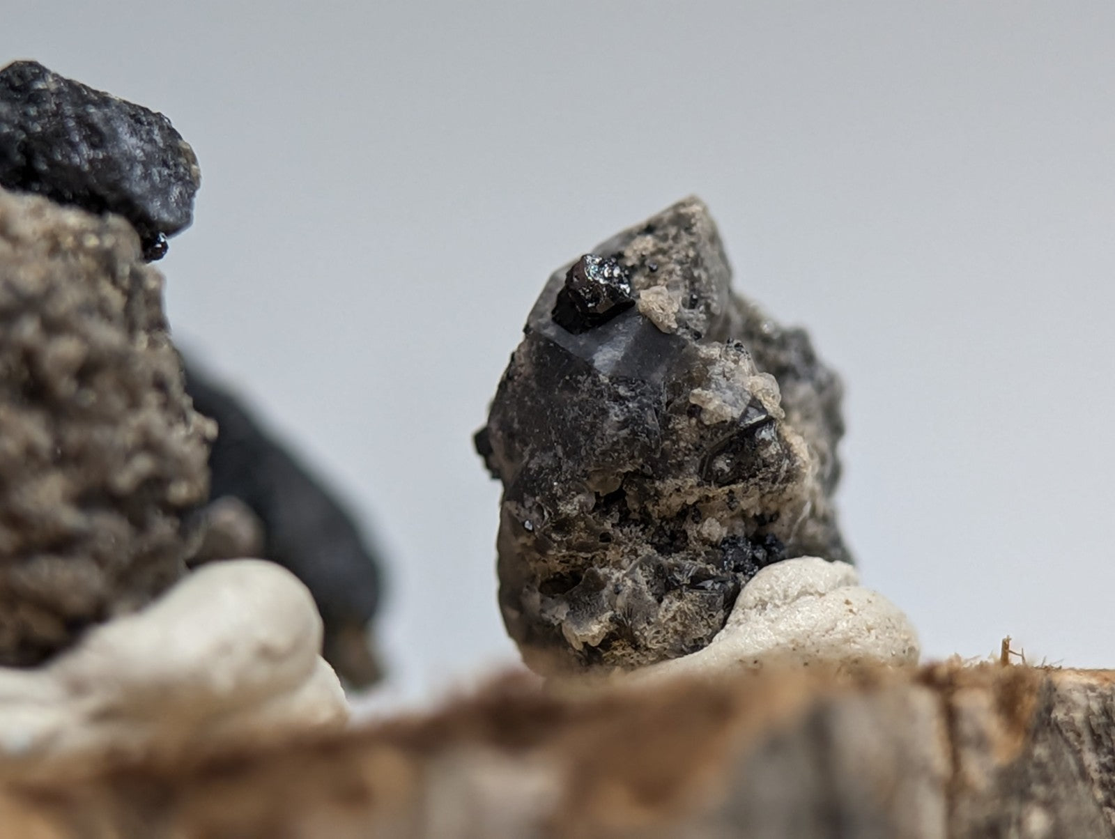 Set of 3 brookite and smoky quartz mineral specimens with dark rough texture and glossy black surface on wood stand