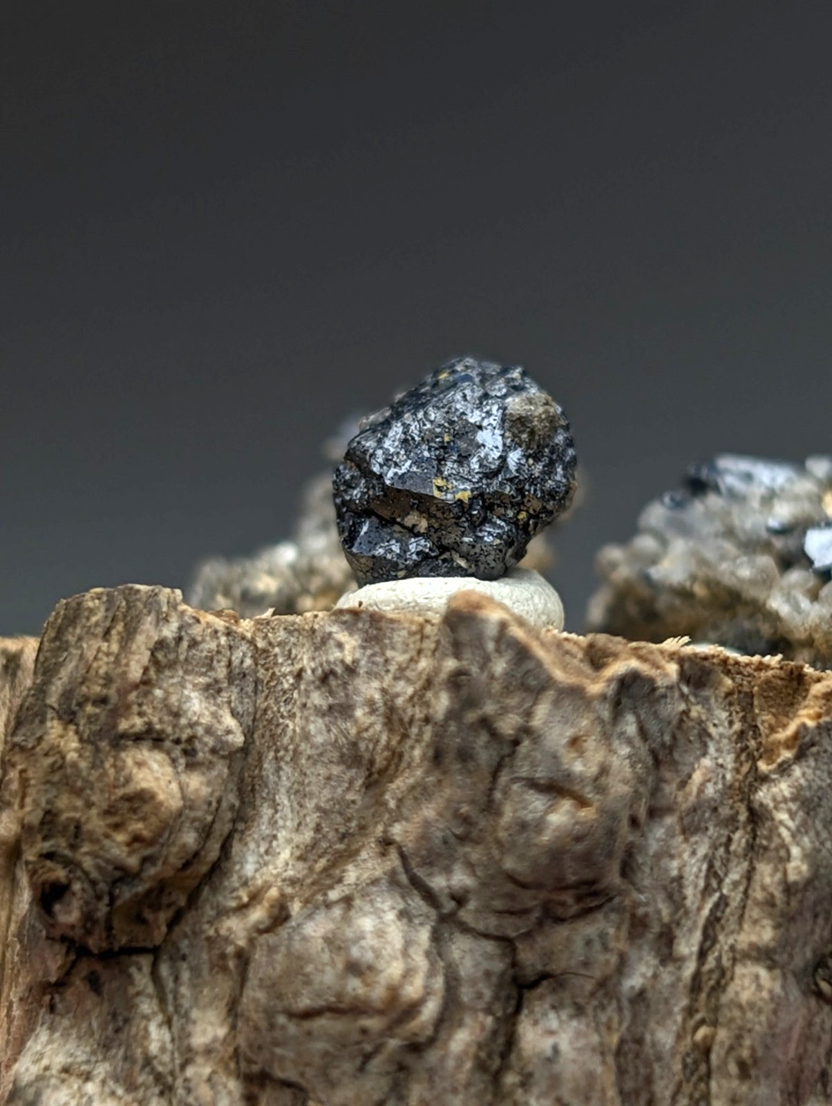 A dark rough-textured brookite and smoky quartz mineral with mottled black and gray on a wooden stand from magnet cove arkansas