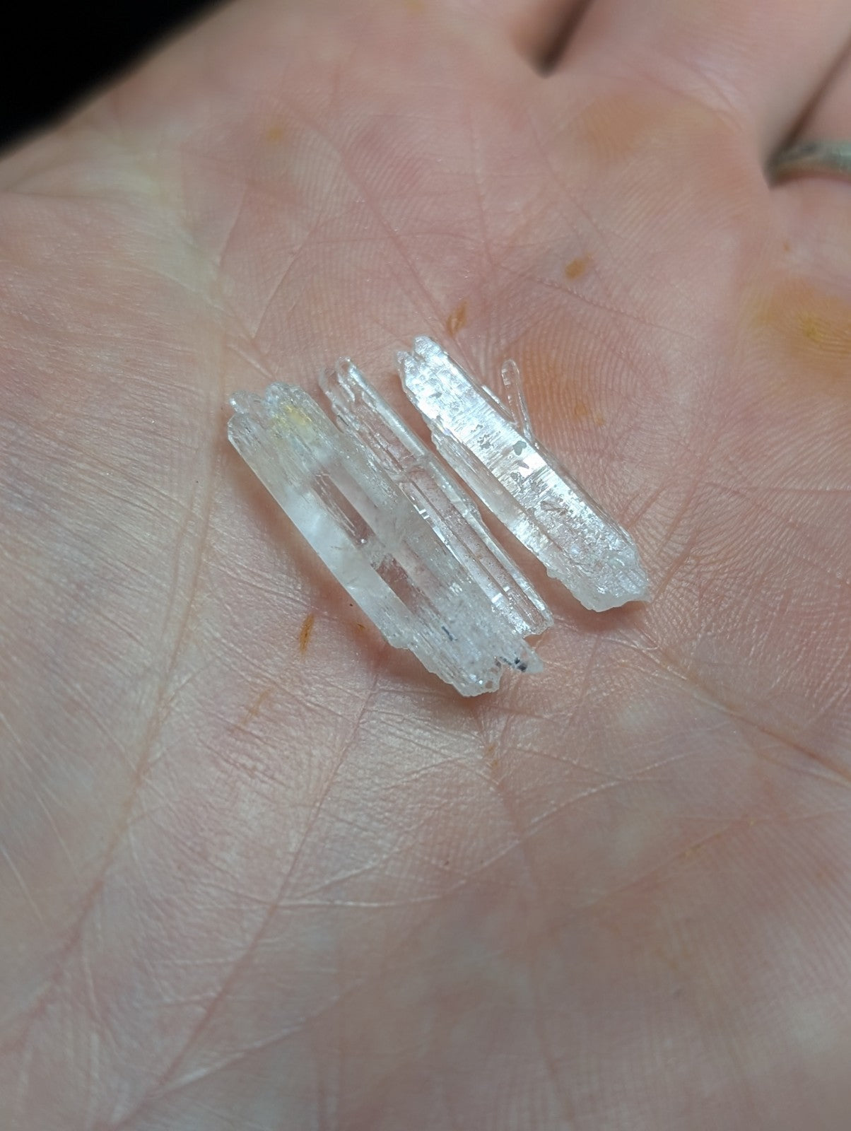 Clear, translucent quartz crystals with sharp edges and pointed tips rest in the palm.