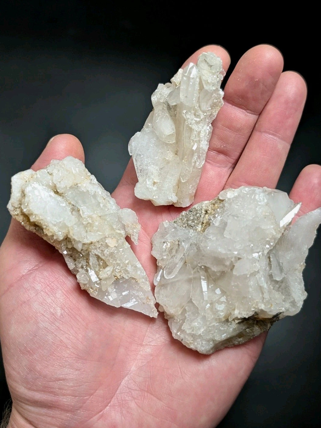 Three translucent white quartz crystal clusters with jagged, faceted surfaces and some earthy brownish matrix.