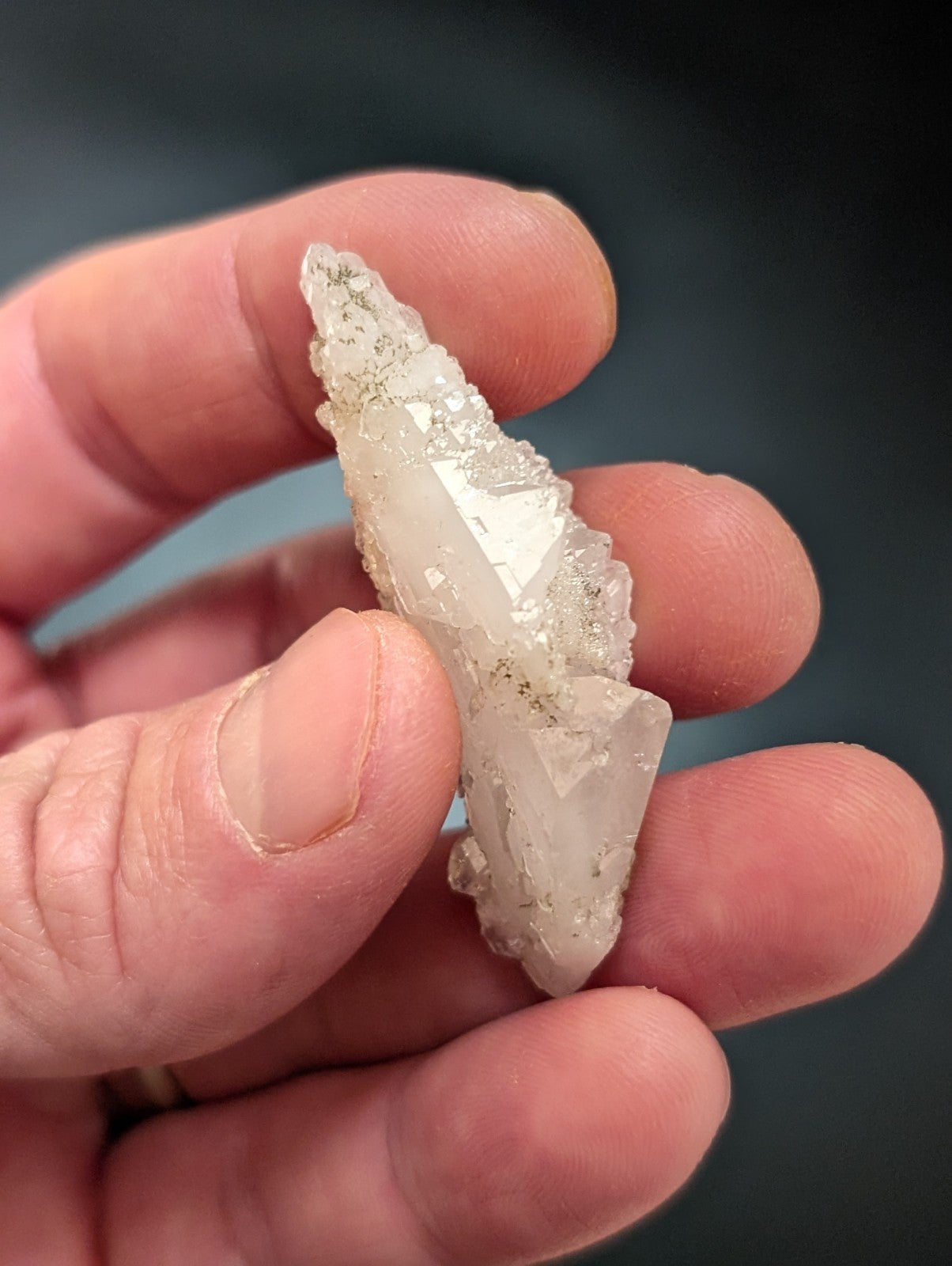 A translucent, pale quartz crystal with a pointed tip and rough, faceted surfaces.