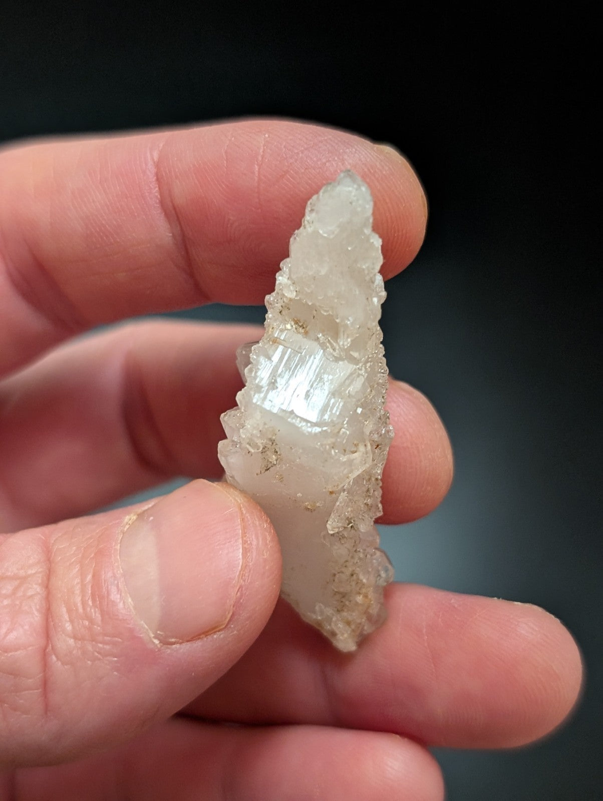 A translucent, pale white mineral crystal with a pointed tip and visible internal striations.