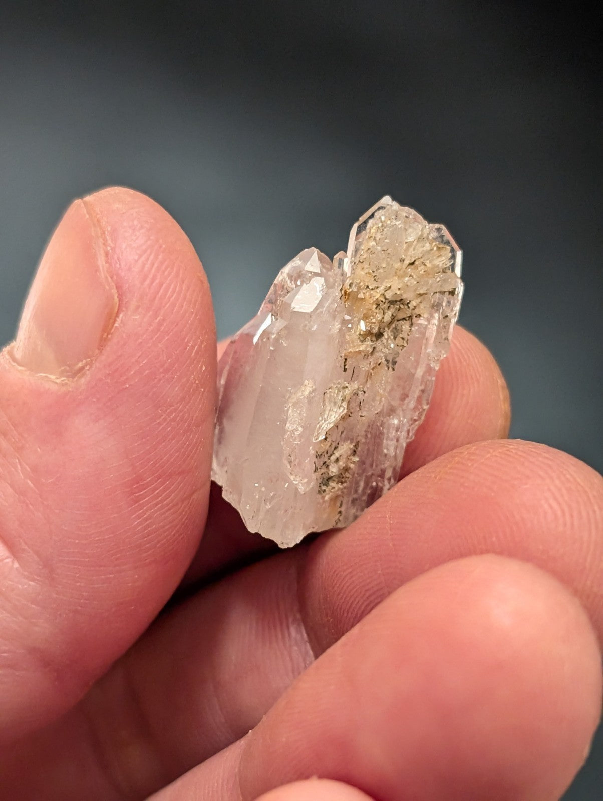 A translucent quartz crystal with golden inclusions, held gently between fingers.