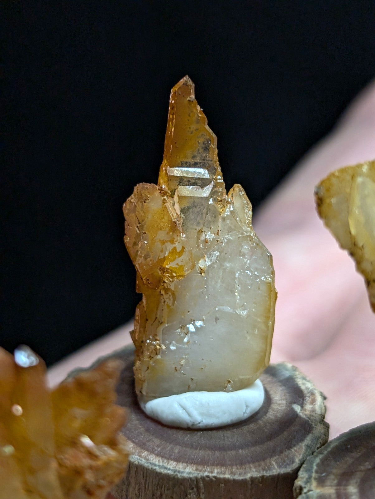 A translucent amber-colored crystal with a sharp, pointed tip and rough, faceted surfaces sits atop a circular wooden base.