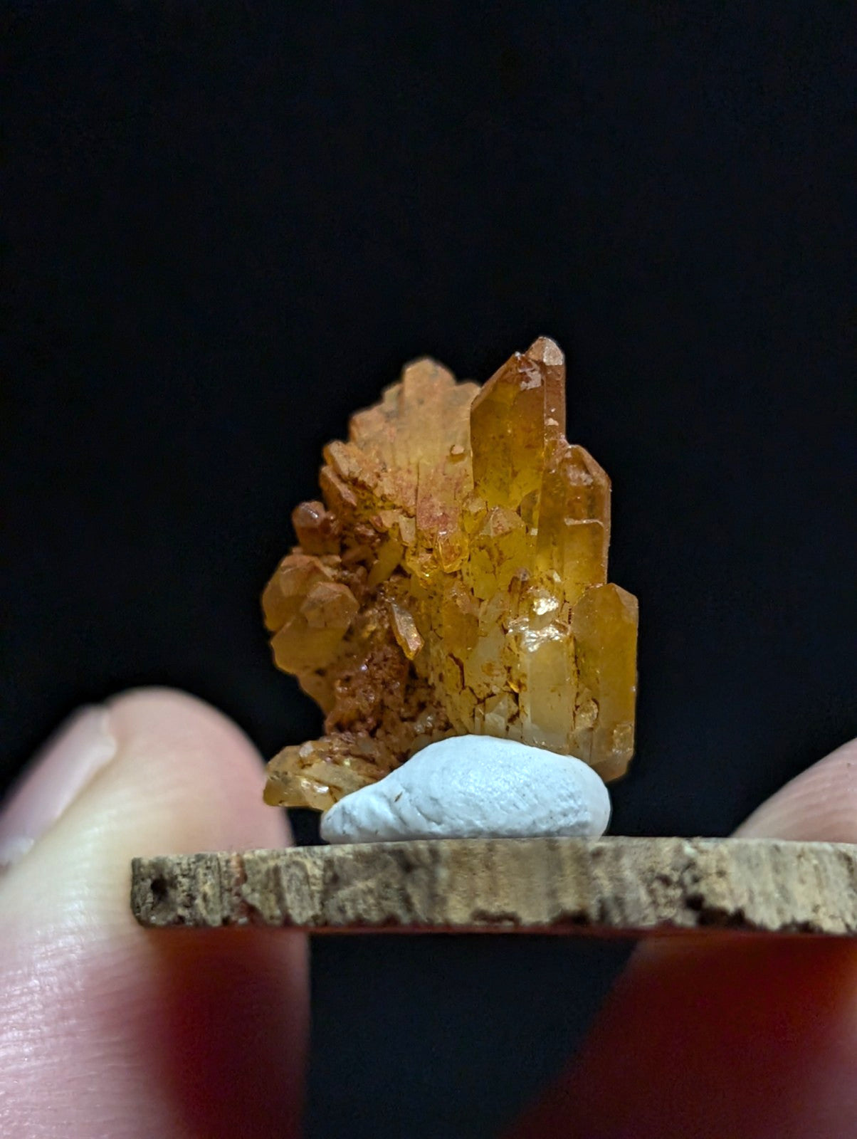 A translucent amber-colored crystal cluster with sharp, faceted points and a rougher brownish base.
