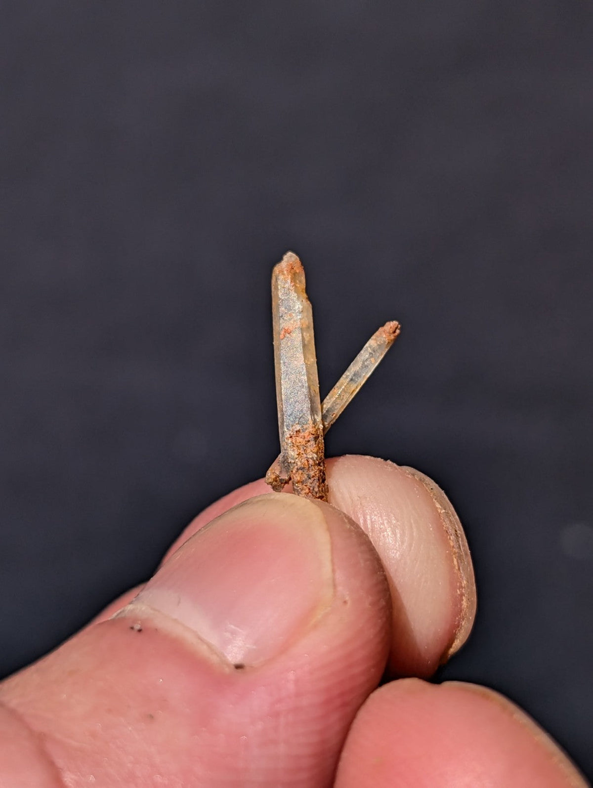 A weathered, rust-speckled metal nail with a pointed tip and two intersecting prongs.