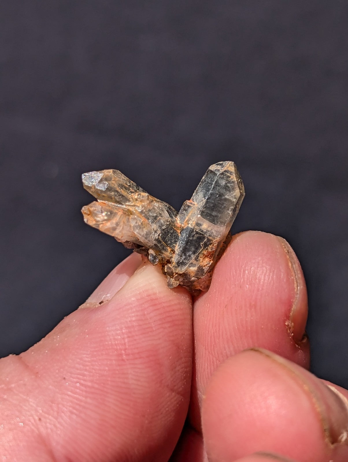 A translucent, multi-faceted quartz crystal cluster with a mix of clear and amber hues, held delicately between fingers.