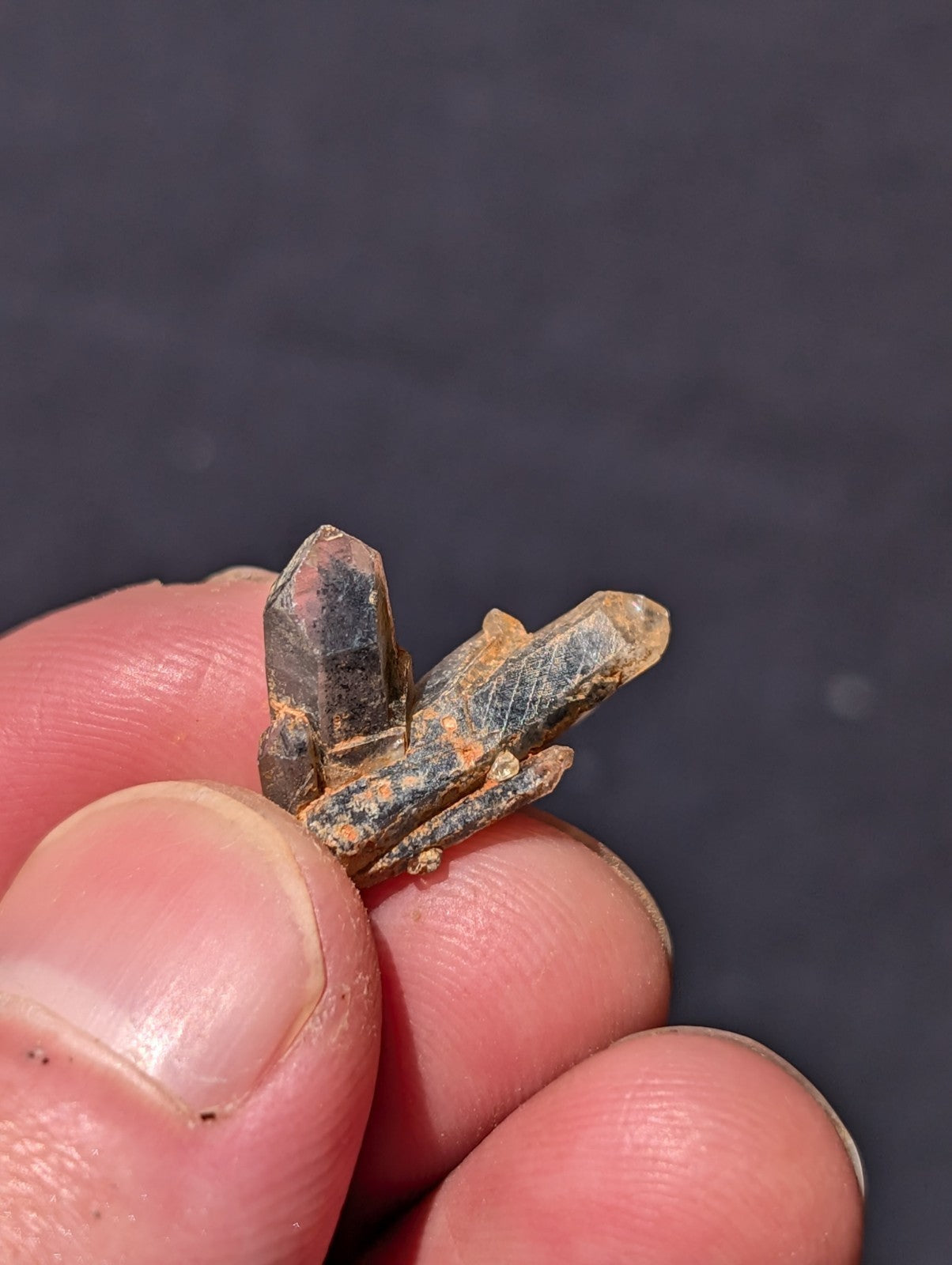 A cluster of translucent quartz crystals with a mix of clear and amber-hued facets, held delicately between fingers.