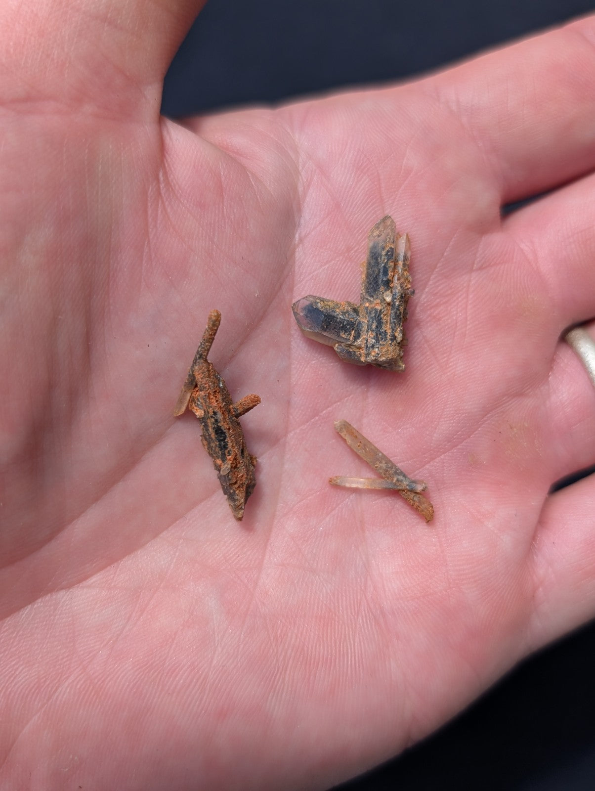 A hand holds three small, rusted metal fragments with a weathered orange-brown patina and visible crystalline structures.