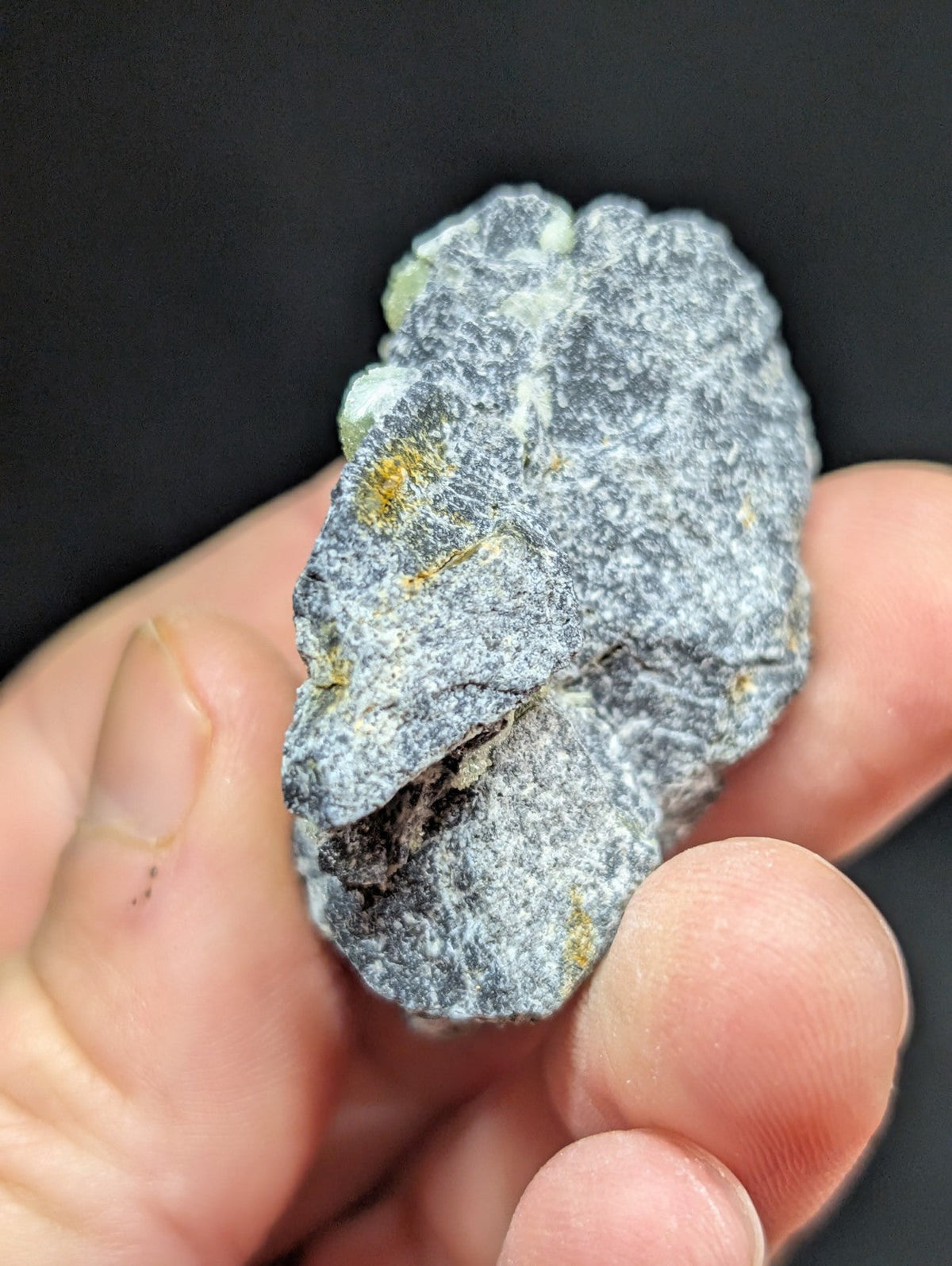 A gray, textured mineral specimen with subtle yellow and white inclusions.