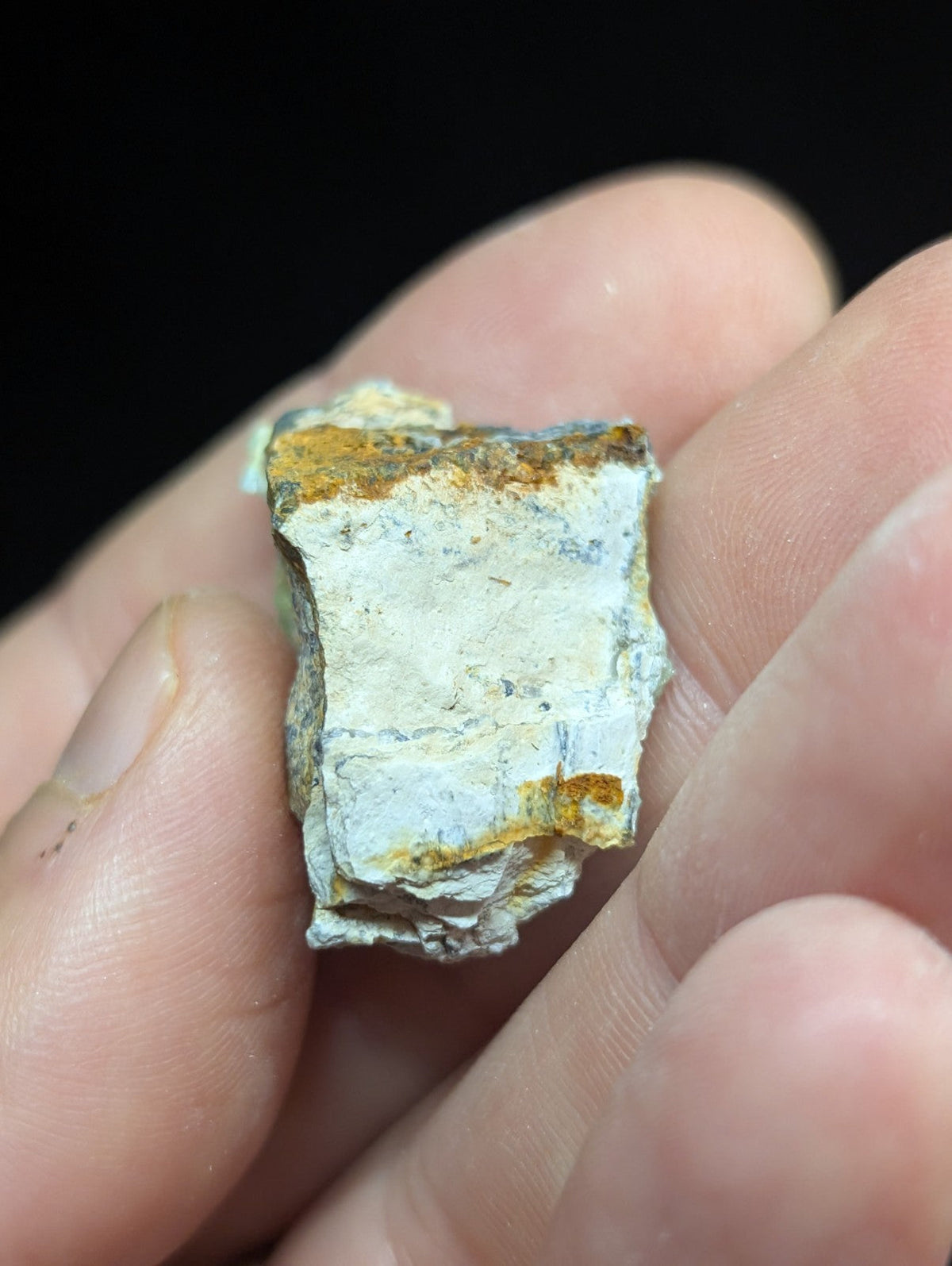 A rough, irregularly shaped mineral fragment with a white base and patches of orange-brown oxidation.