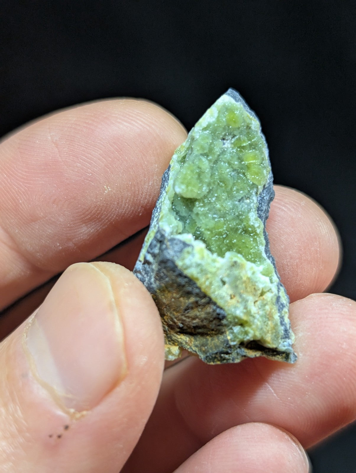 A jagged, triangular piece of green mineral with a rough, crystalline surface and dark gray matrix.