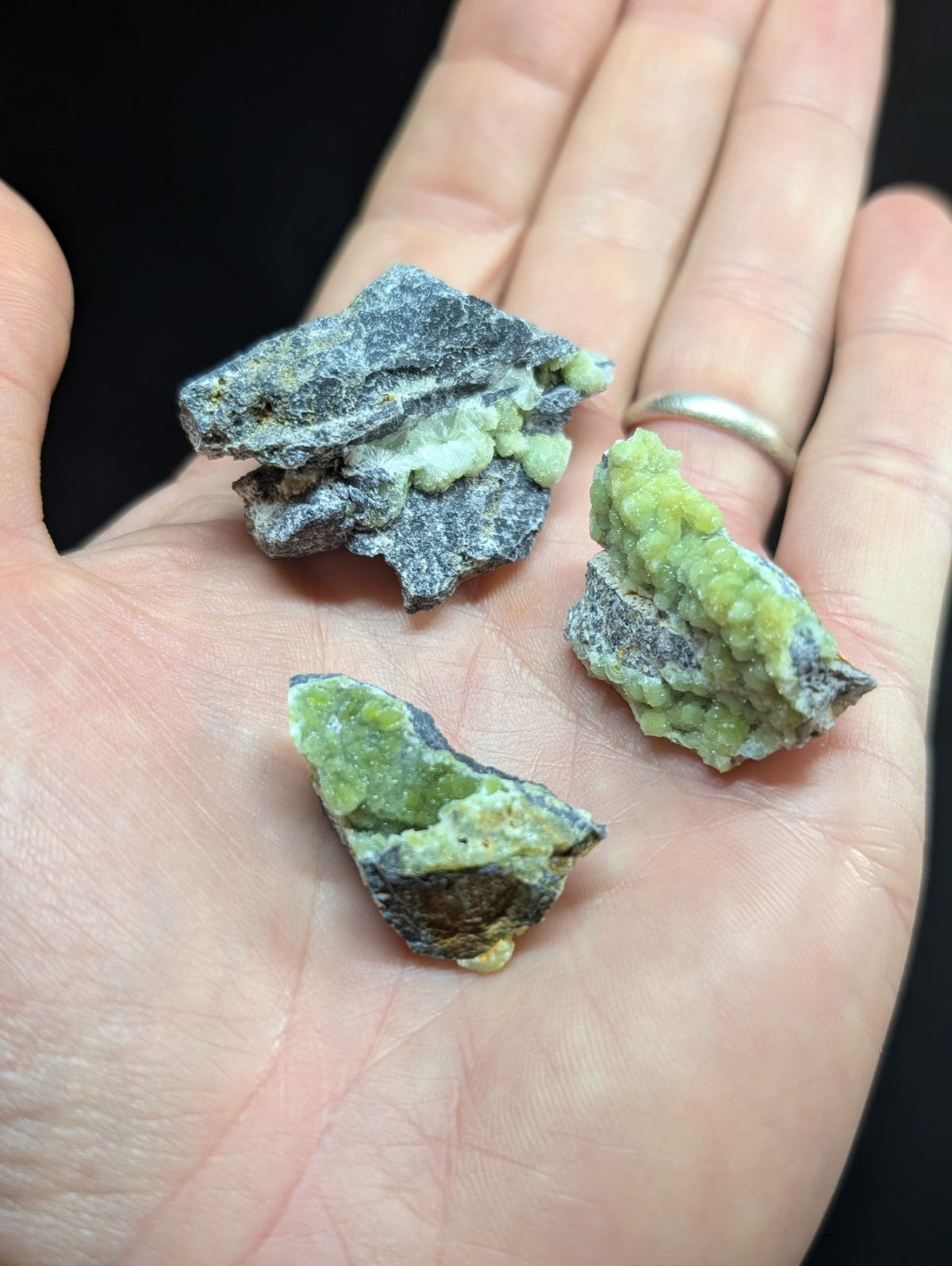 Three irregularly shaped, rough-textured mineral specimens with a mix of dark gray and vibrant green hues.
