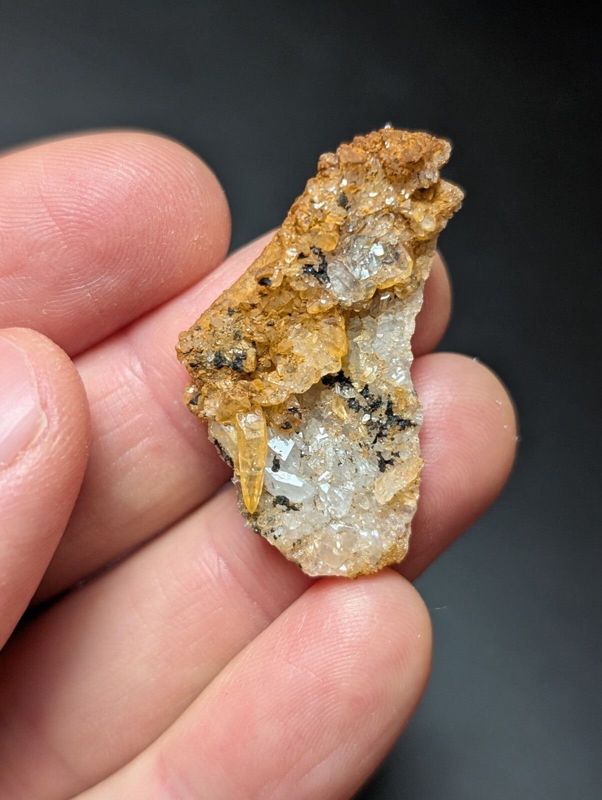 A hand holds a rough, irregularly shaped mineral specimen featuring translucent yellow and clear crystal formations embedded in an orange-brown matrix.