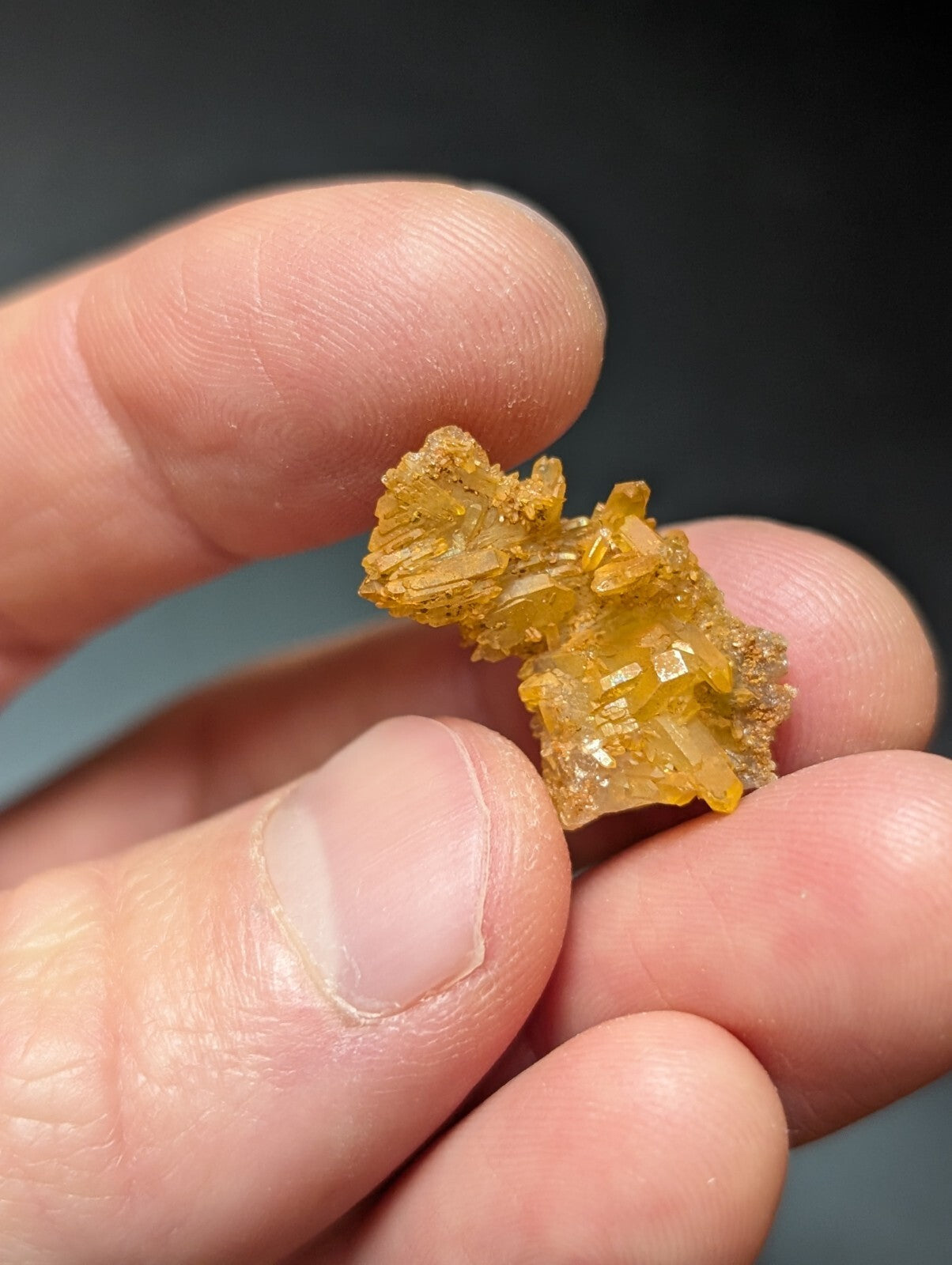 A cluster of translucent golden-yellow crystals with jagged, faceted surfaces held between fingers.
