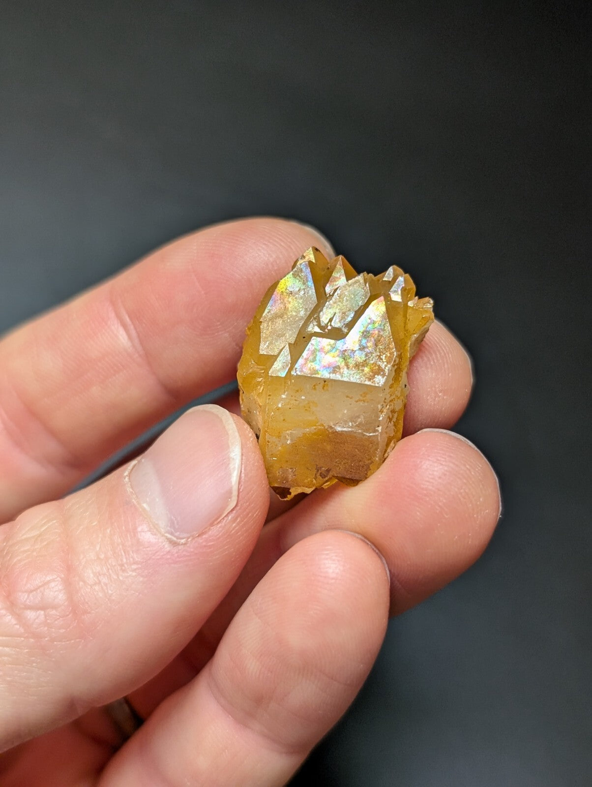 A golden-yellow, faceted crystal cluster with iridescent flashes of rainbow hues.