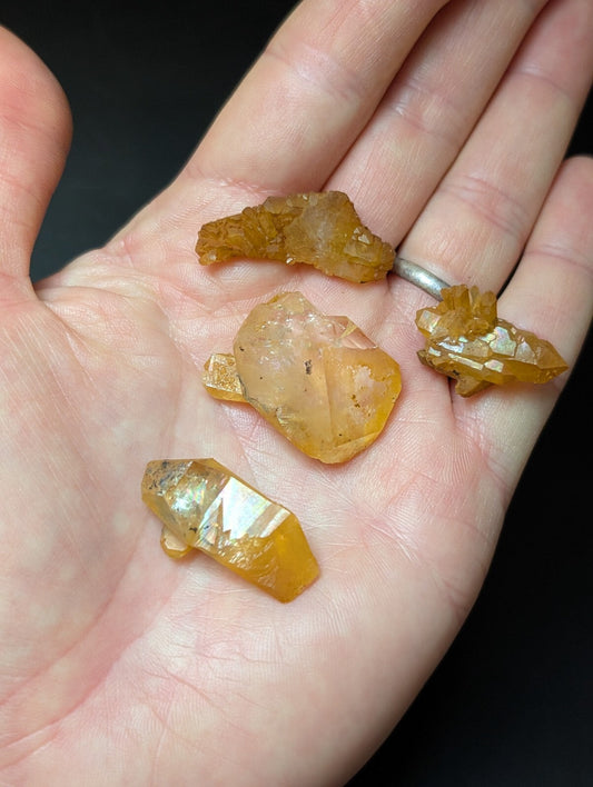 A hand holds four translucent amber-colored crystal specimens with jagged, faceted edges and natural mineral inclusions.