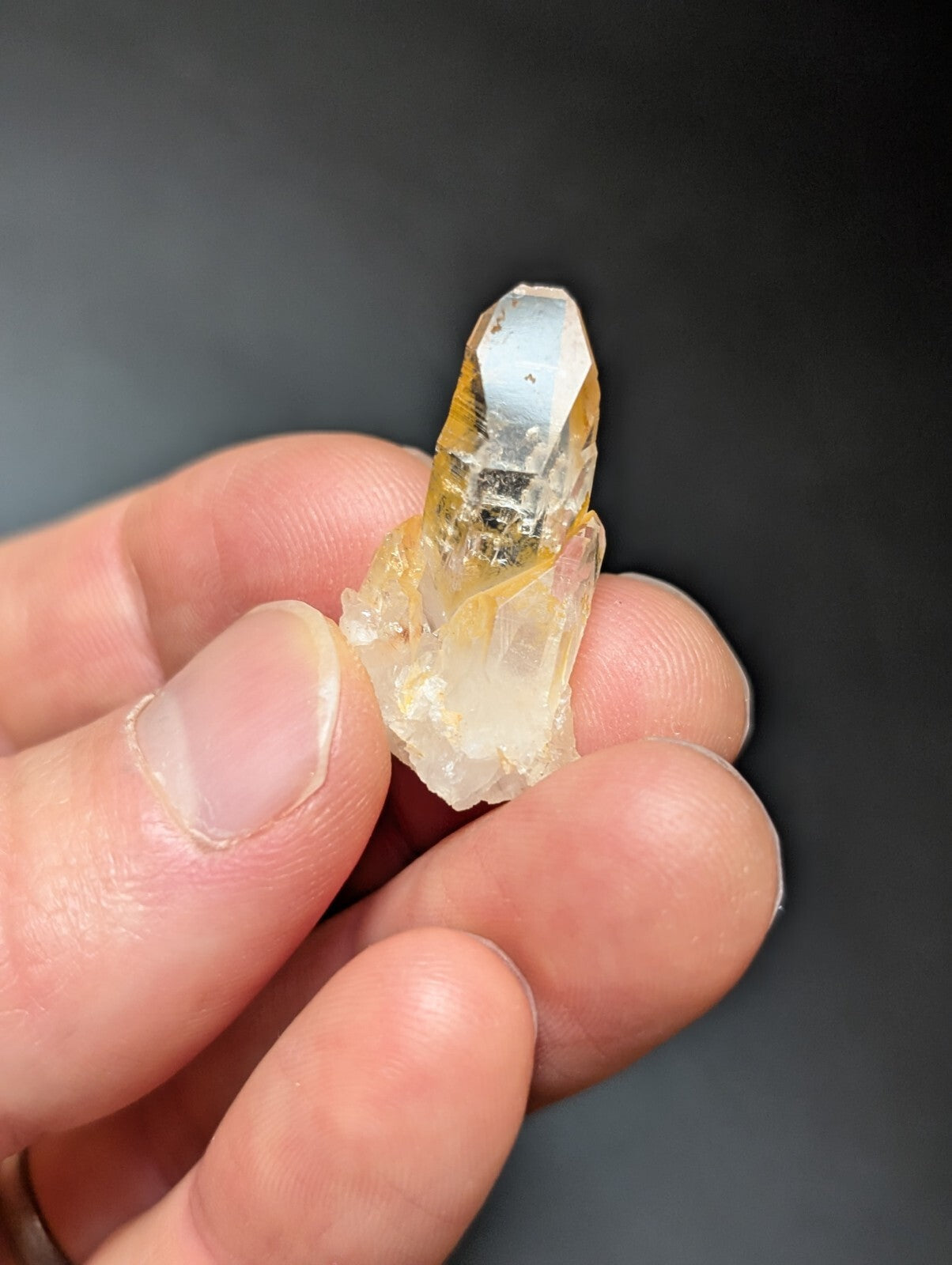 A translucent yellowish quartz crystal with a pointed tip and visible internal inclusions, held gently between fingers.