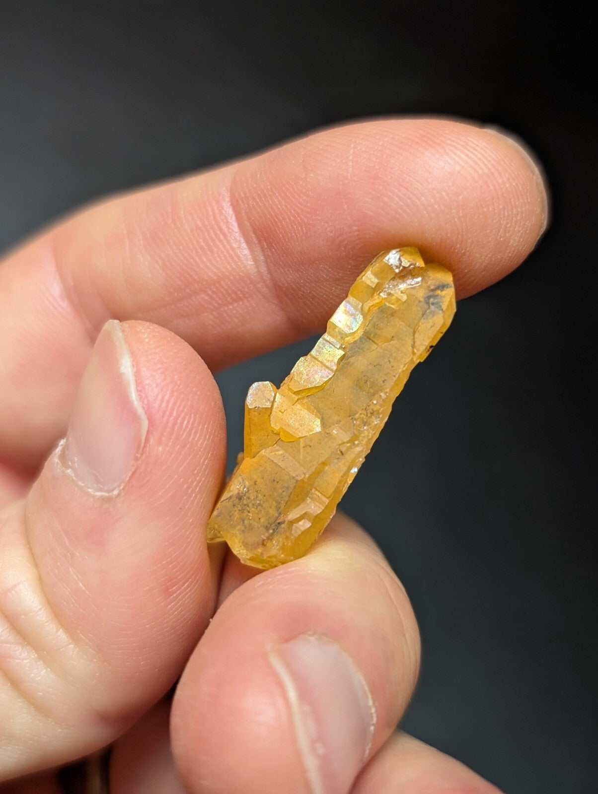 A translucent golden-yellow crystal with jagged, faceted edges held between fingers.