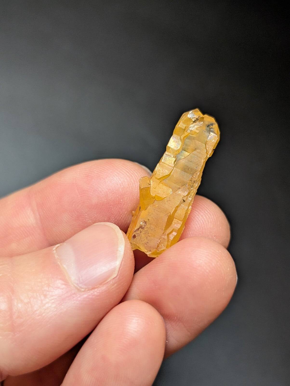 A translucent golden-yellow crystal with visible striations and natural imperfections, held gently between fingers.