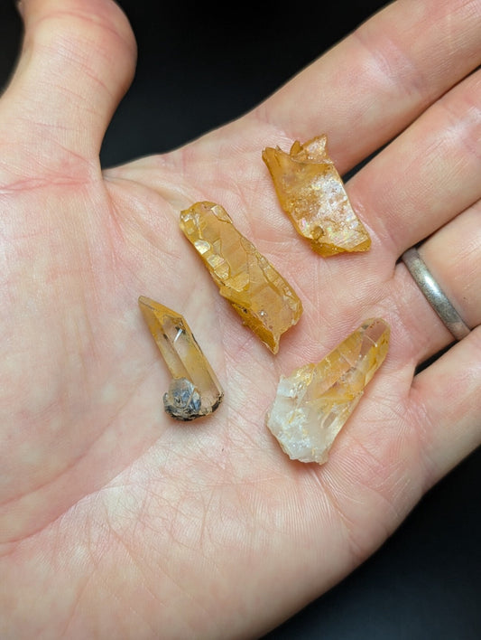 A hand holds several translucent amber-colored crystal fragments with jagged edges and natural mineral inclusions.
