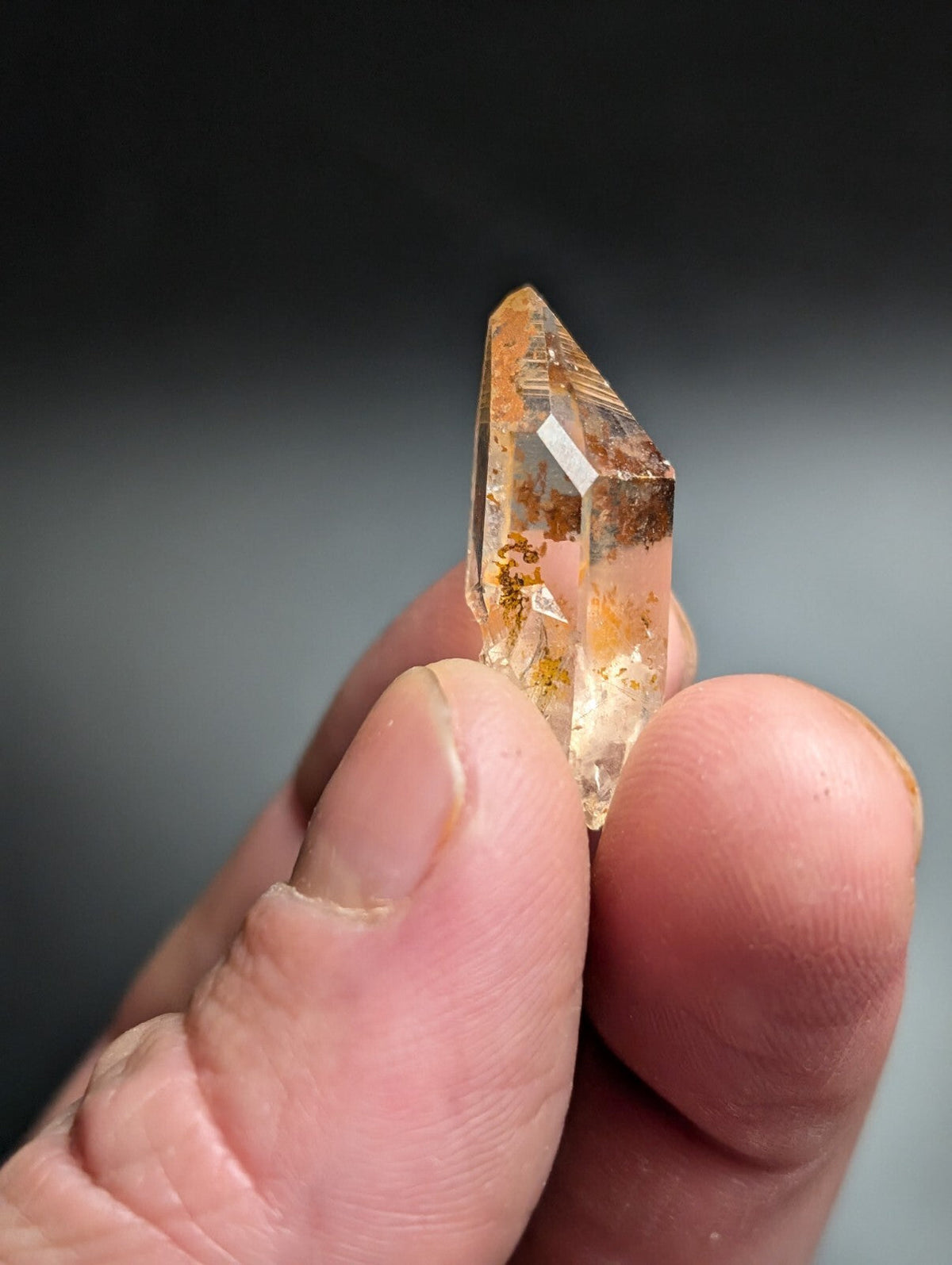 A translucent amber-colored quartz crystal with golden inclusions and a pointed, faceted tip.
