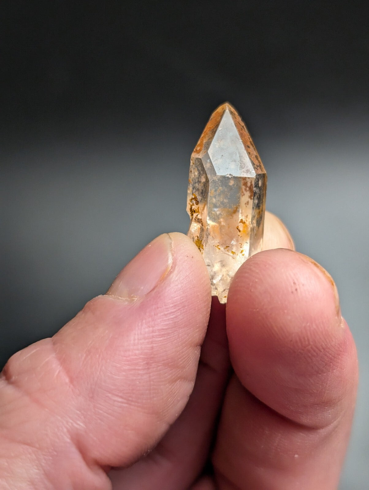 A translucent golden-yellow quartz crystal with natural inclusions, held delicately between fingers.
