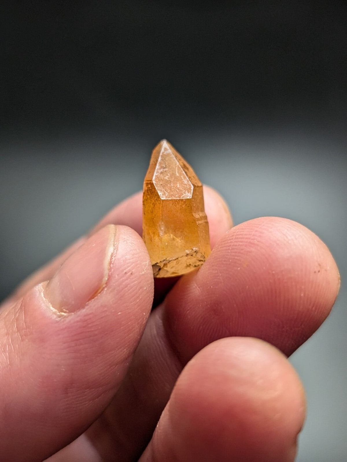 A translucent amber-colored crystal with a pointed, faceted tip and natural inclusions at its base.