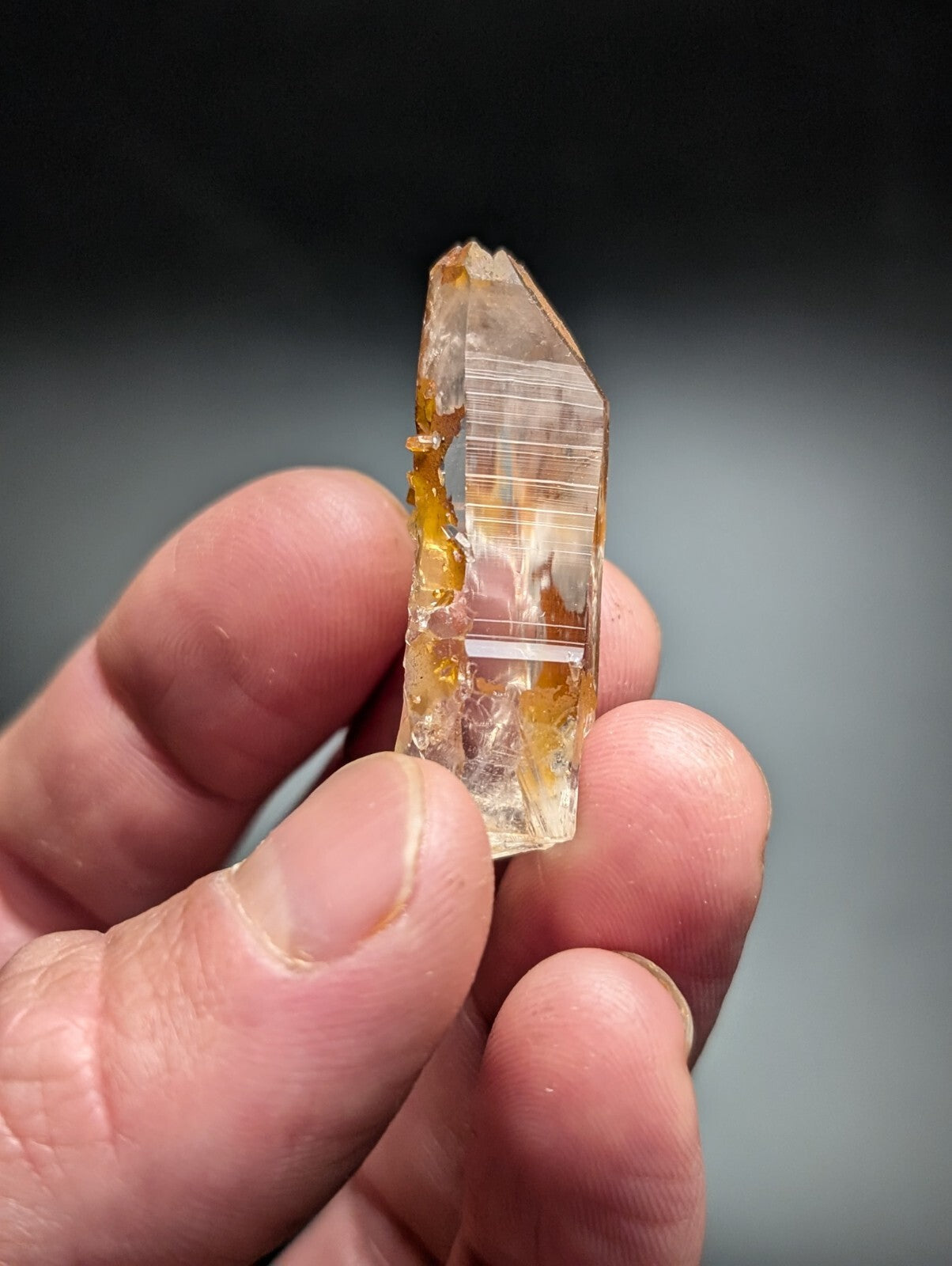 A translucent golden-yellow quartz crystal with visible internal striations and a pointed tip, held gently between fingers.