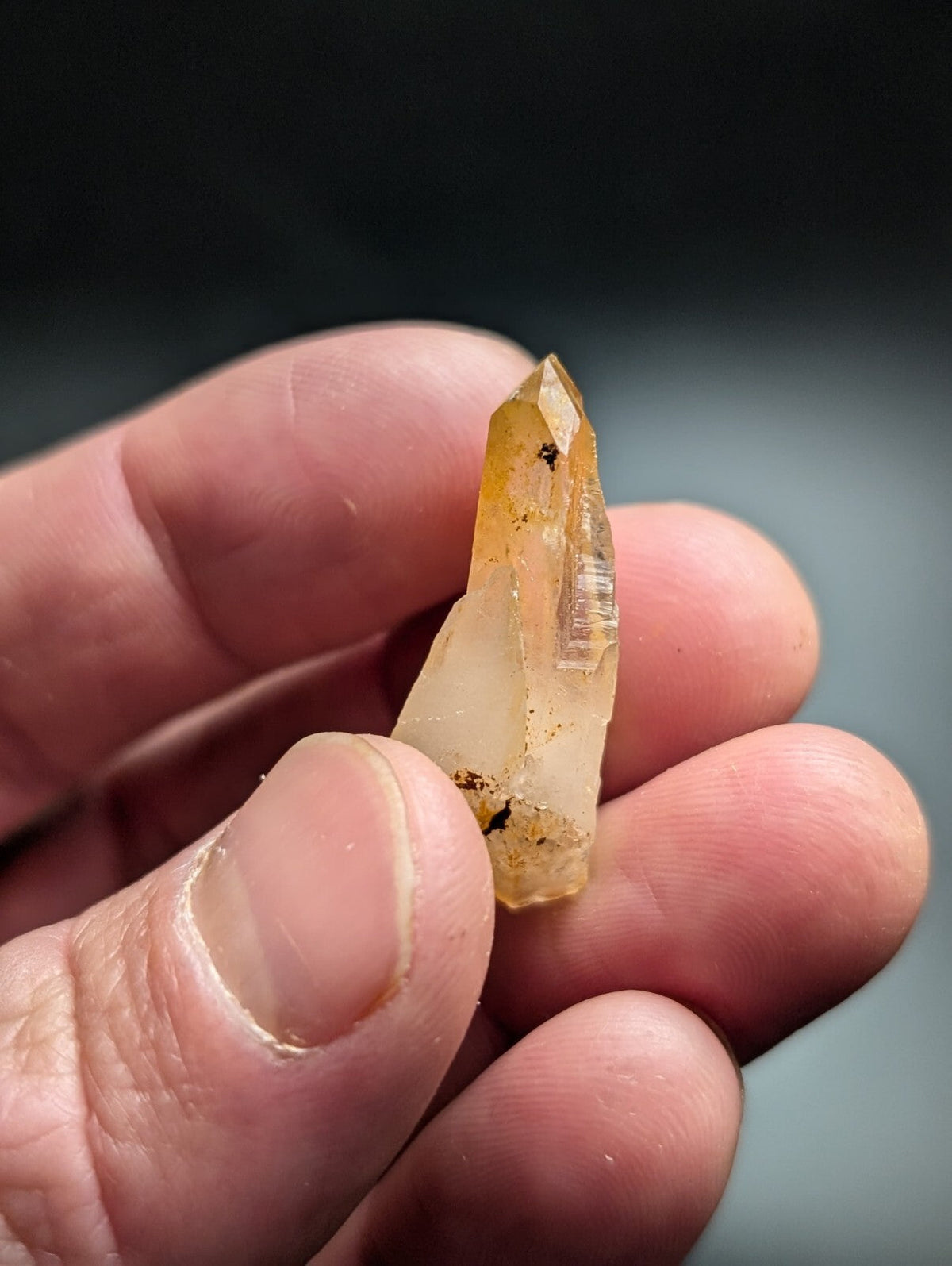 A translucent yellowish quartz crystal with a pointed tip and natural inclusions, held gently between fingers.