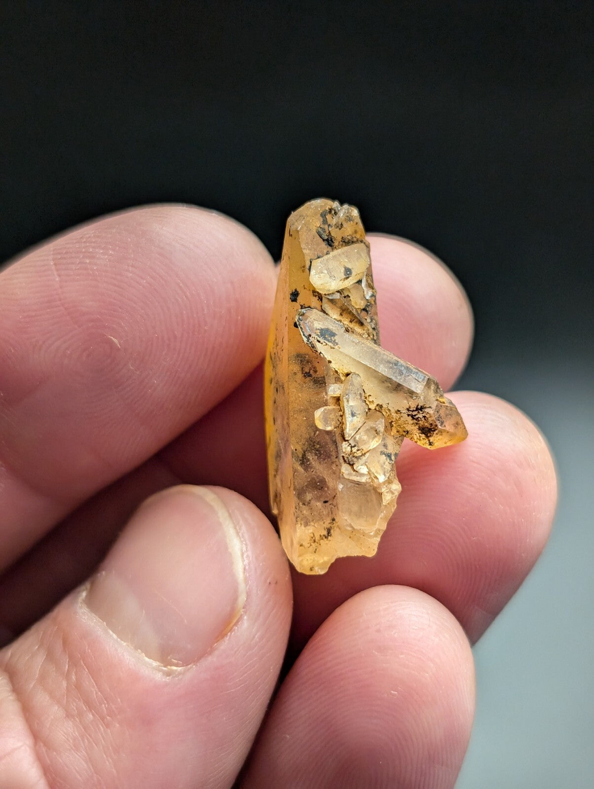 A translucent amber-colored crystal cluster with clear, pointed facets and dark mineral inclusions.