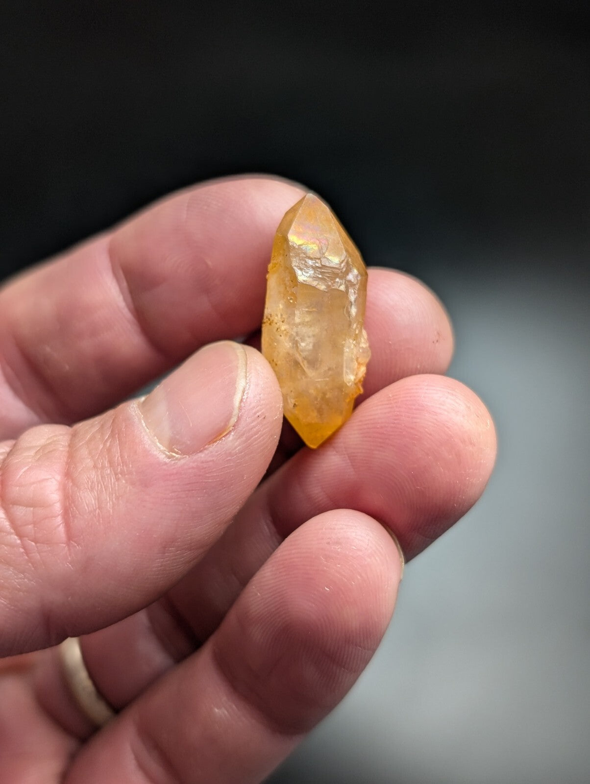 A translucent golden-yellow crystal with a pointed tip and natural facets, held gently in someone’s hand.