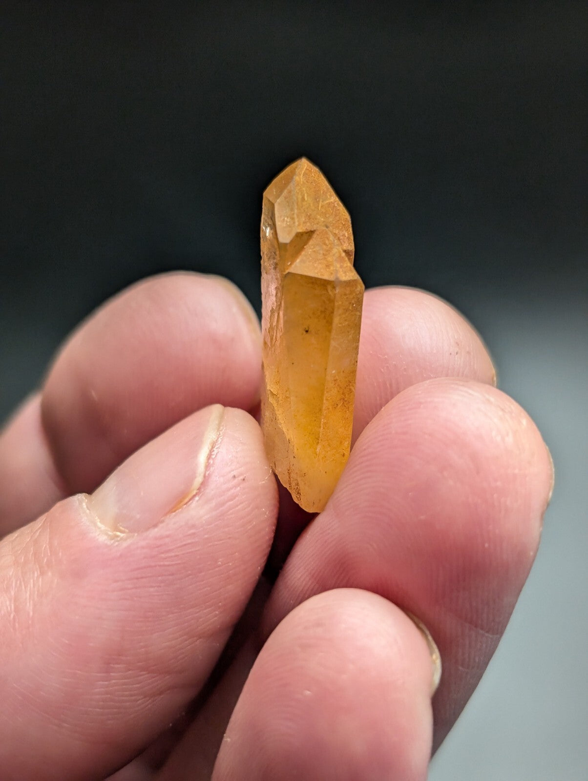 A translucent golden-yellow crystal with a pointed, faceted tip and smooth sides.
