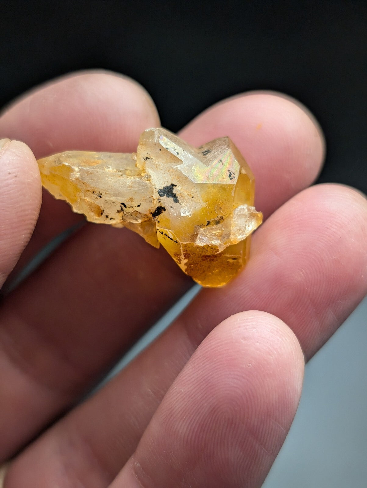 A translucent amber-colored crystal cluster with sharp, angular facets and subtle black inclusions.