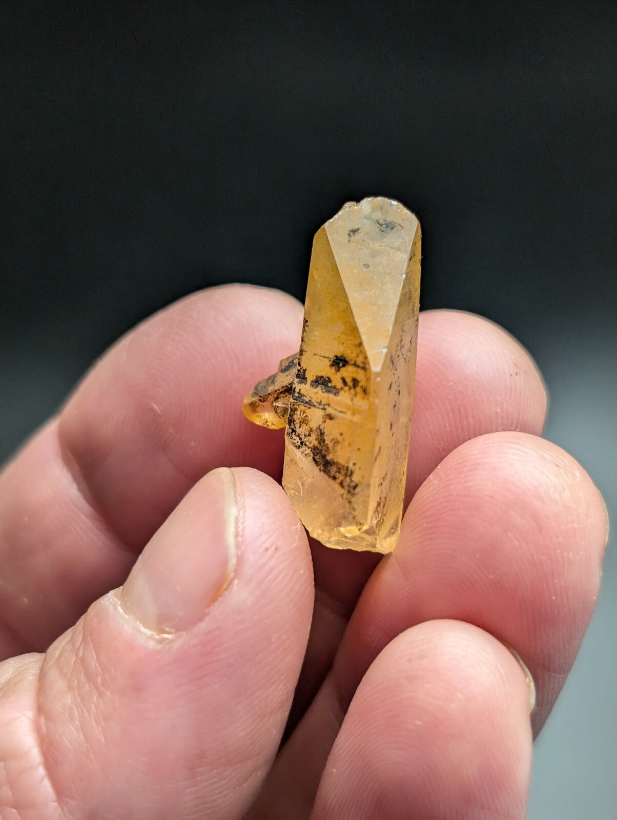 A translucent yellow crystal with a faceted, pointed top and dark inclusions along its surface.