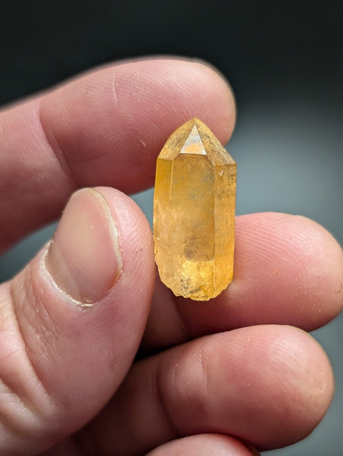 A translucent golden-yellow citrine crystal with a pointed, faceted top and natural imperfections along its base.