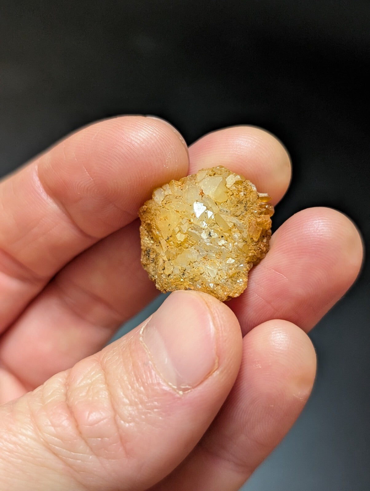 A golden-yellow, translucent crystal cluster with a rough, faceted surface held gently in someone’s hand.