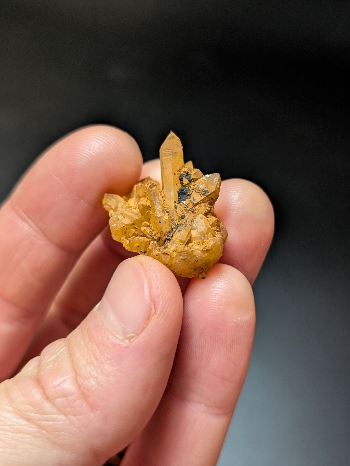 A translucent golden-yellow crystal cluster with a prominent central spike, held gently in someone’s hand.