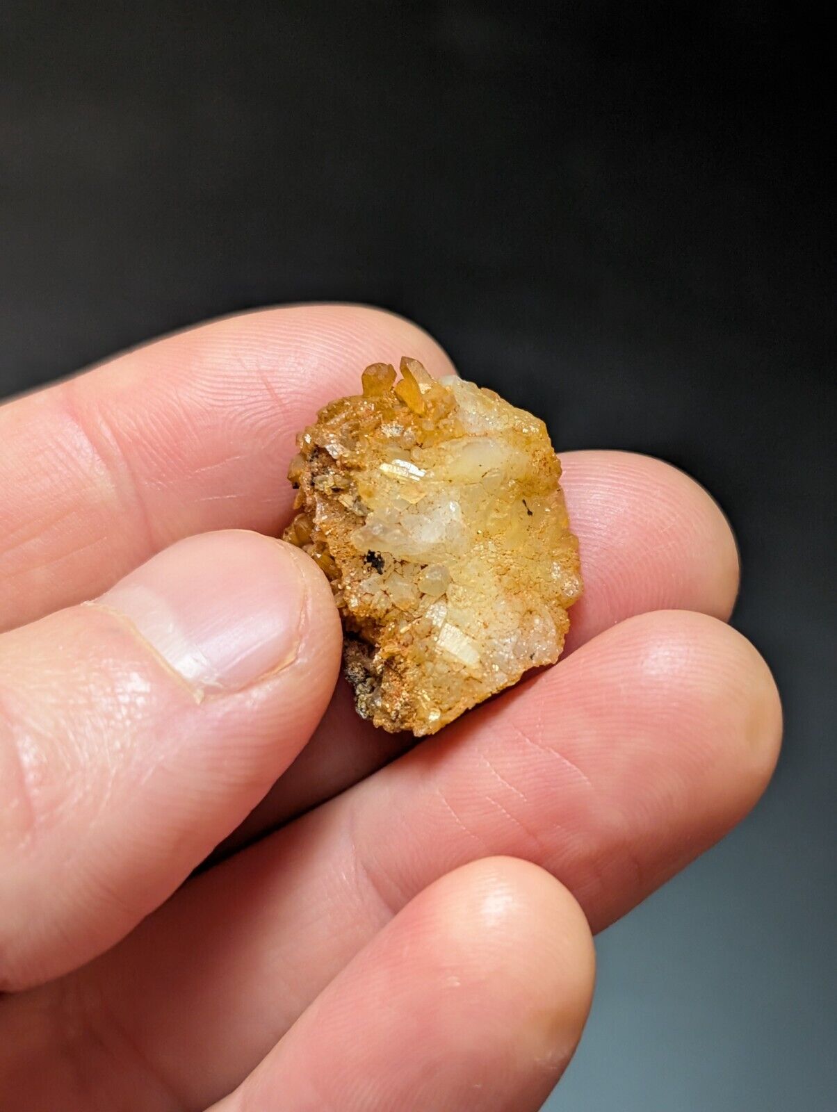 Hand holding a rough, yellowish mineral specimen.