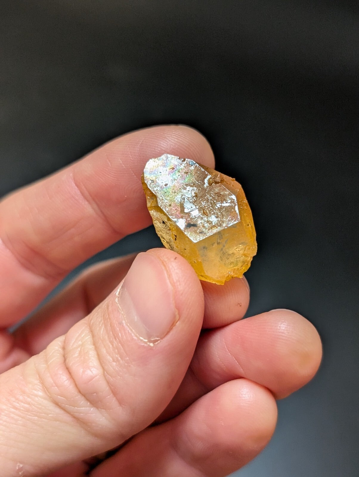A translucent amber-colored mineral specimen with a metallic, iridescent patch on its surface.