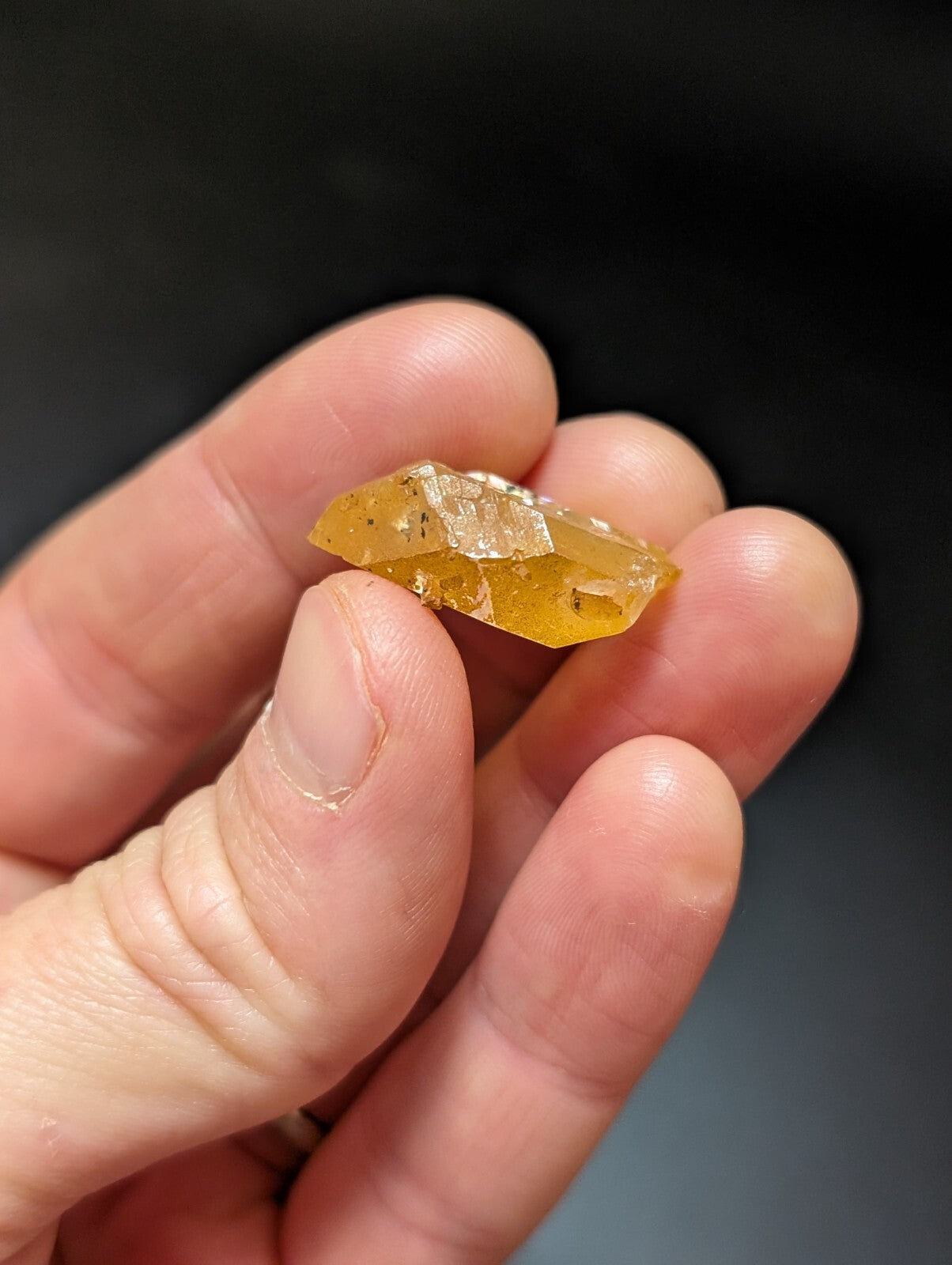 A translucent amber-colored crystal with a faceted, geometric shape and subtle internal inclusions.