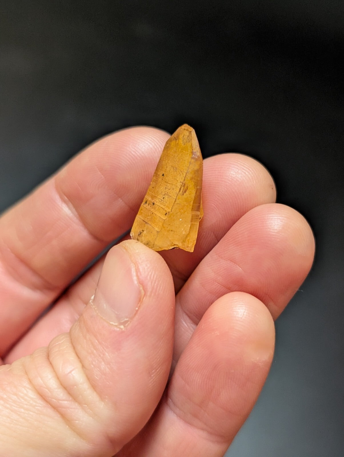 A translucent amber-colored crystal with a pointed, faceted tip and natural striations.