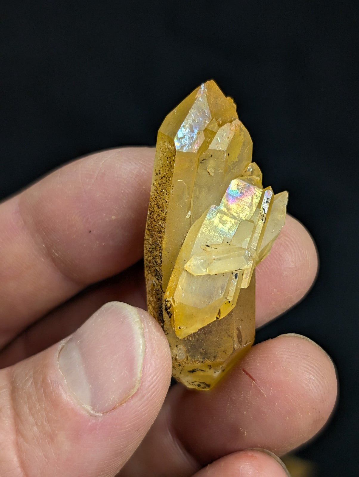 A translucent golden-yellow crystal cluster with iridescent facets, held gently in a hand.