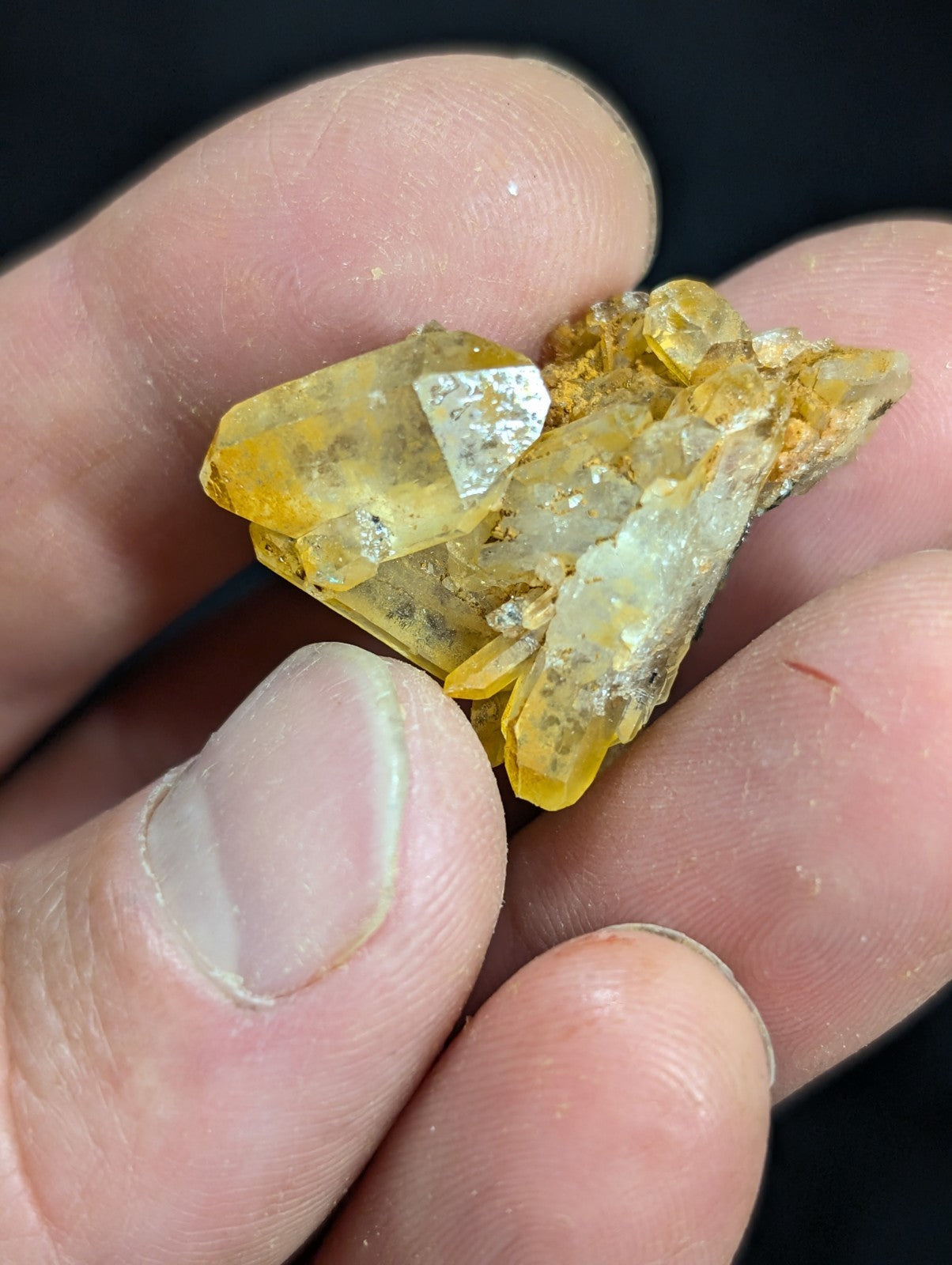 A cluster of translucent yellow crystals with a few white crystalline inclusions, held gently between fingers.