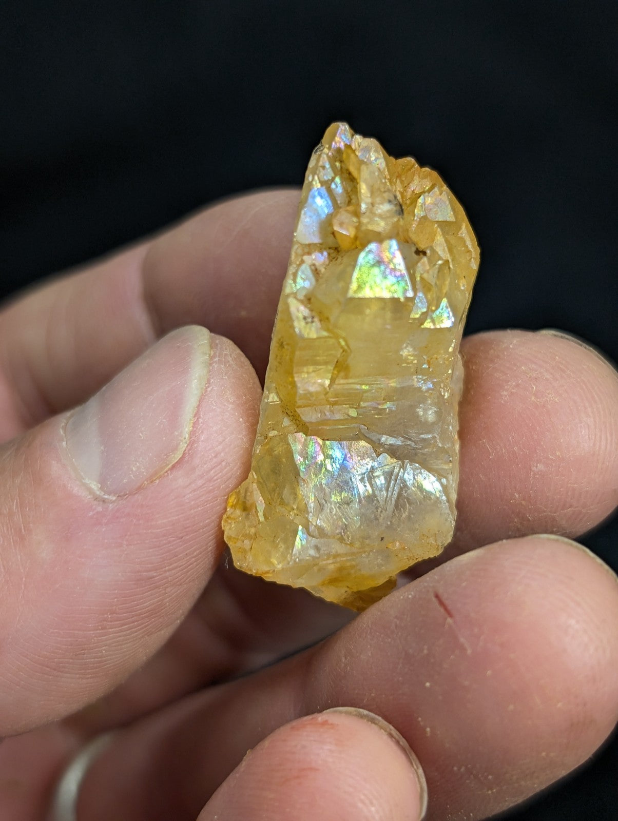 A translucent golden-yellow crystal with iridescent facets, held gently in a hand.